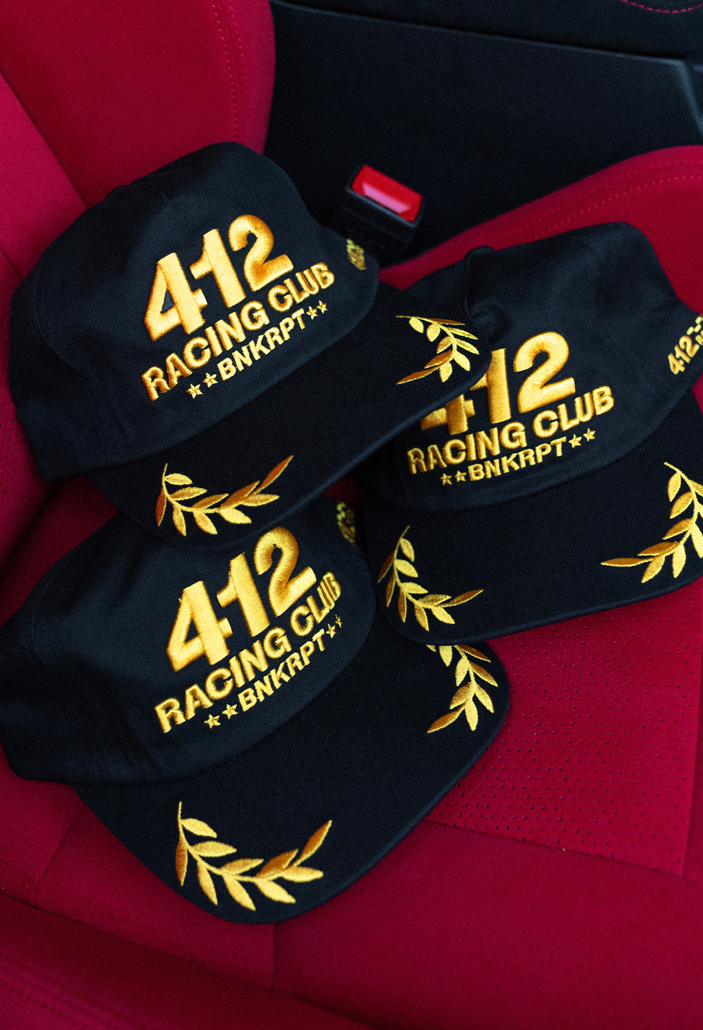 Black caps with gold '412 Racing Club' text on a red surface