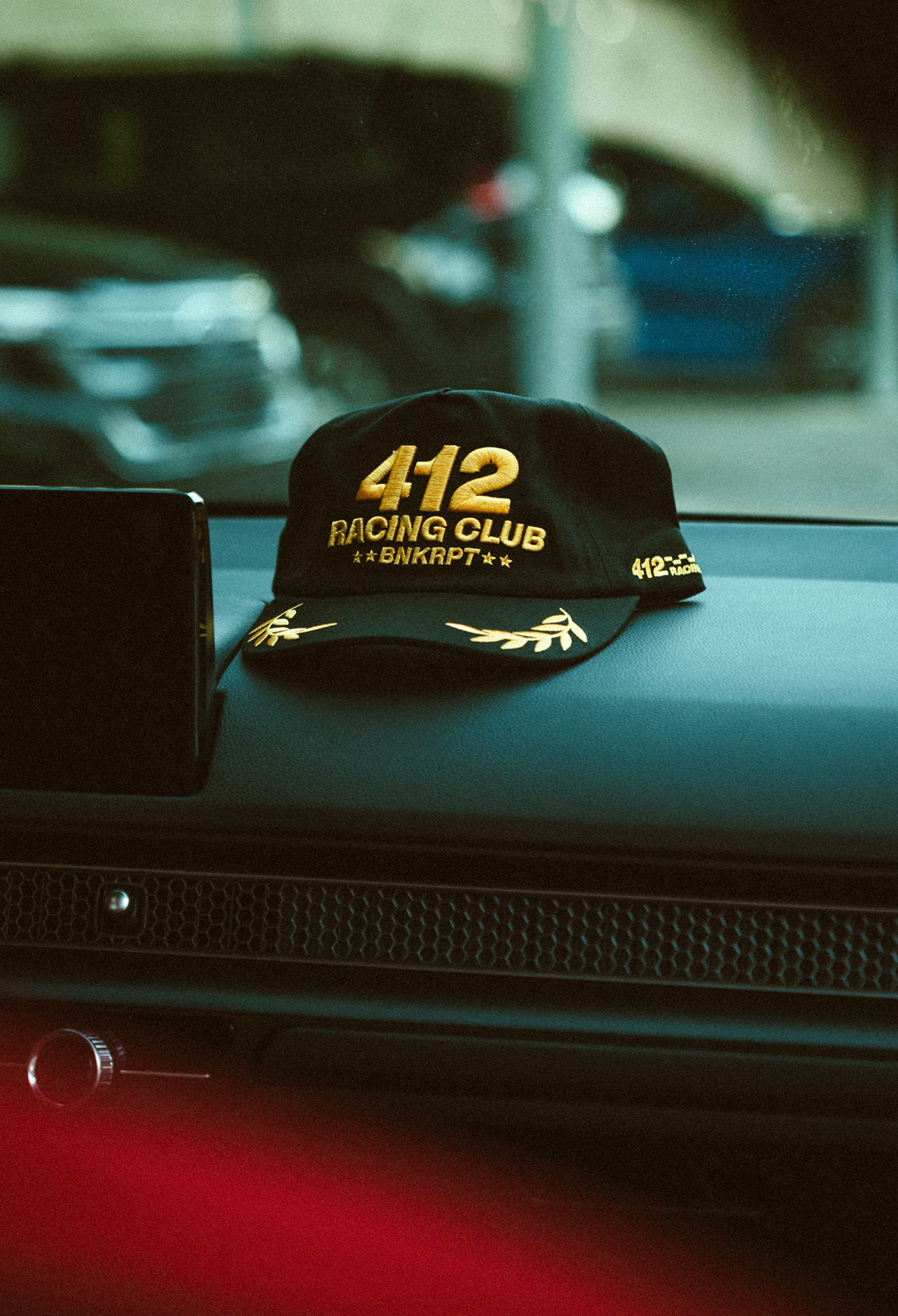 Black cap with gold text 412 RACING CLUB on a car dashboard